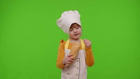 Child-girl-kid-dressed-in-apron-and-hat-like-chef-cook-eating-fresh-tasty-baguette,-making-faces