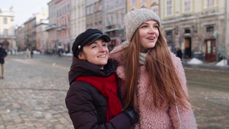 Dos-Mujeres-Turistas-Sonrientes-Caminando-Juntas-Por-Las-Calles-De-La-Ciudad,-Una-Pareja-Familiar-Hablando,-Abrazándose