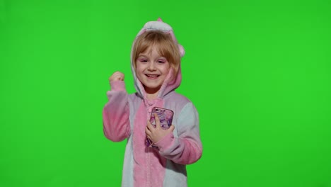 Excited-little-child-girl-in-unicorn-pajamas-using-mobile-cell-phone,-found-out-great-big-win-news