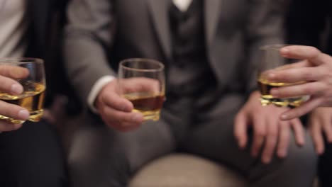 Company-of-grooms-friends-holding-and-clinking-glasses-of-alcoholic-whiskey-drinks-in-their-hands