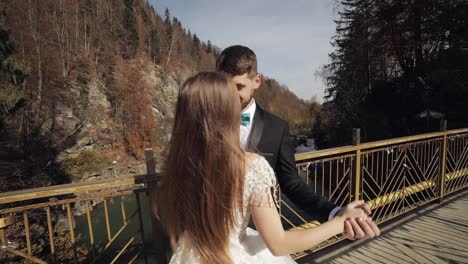 Newlyweds.-Caucasian-groom-with-bride-dancing-on-a-bridge-over-a-mountain-river