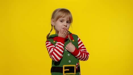 Shy-shamed-child-girl-in-Christmas-elf-Santa-helper-costume-posing-looking-camera,-blows-air-kiss