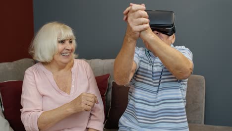 Senior-man-playing-game-in-virtual-reality-headset-glasses,-woman-laughing-with-him-action-at-home