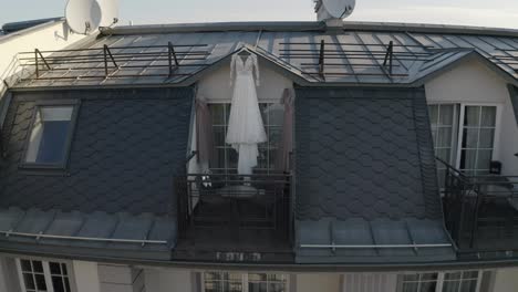 Wedding-gown-dress-hanging-at-balcony-terrace-doorway-waits-for-bride-at-sunny-morning,-aerial-view