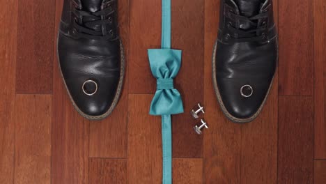 Wedding-rings,-green-grooms-bow-tie,-cufflinks-and-shoes-on-brown-wood-floor