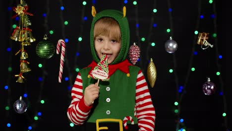 Kid-girl-in-Christmas-elf-Santa-Claus-helper-costume-licking-candy-lollipop-caramel-sweets