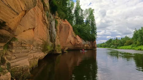 Kayakers-paddle-along-the-serene-river-with-rocky-cliffs-and-lush-greenery-in-Gauja-National-Park,-Latvia