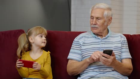 Senior-grandfather-with-child-girl-granddaughter-using-digital-mobile-phone,-playing-games-at-home