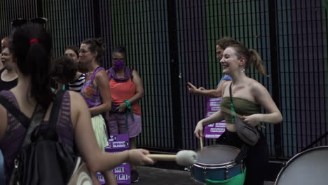 excited-joyful-young-female-protester-plays-drums-and-lifts-arms-to-celebrate-with-group-of-women-at-social-gathering-for-women's-rights