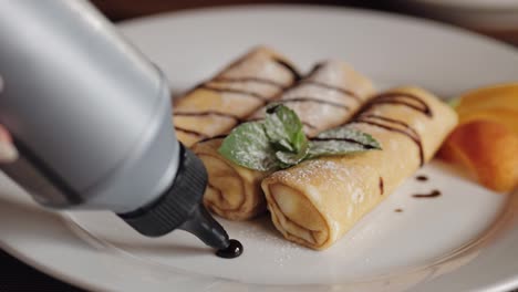 Chef-pouring-chocolate-syrup-on-tasty-delicious-cottage-cheese-peach-pancakes-on-plate-on-table