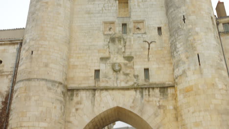 Tilt-up-shot-of-Grosse-Horloge-in-La-Rochelle,-France-with-tourists-exploring-during-daytime