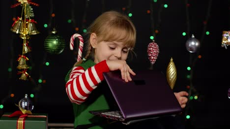 Kid-girl-in-Christmas-elf-costume-doing-shopping-online-using-laptop,-browsing-on-social-media