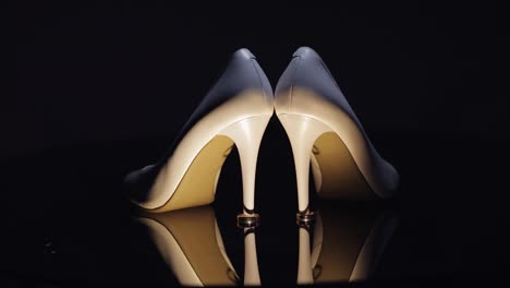 Hermosos-Zapatos-De-Noche-De-Mujer-De-Color-Crema-Yacen-En-El-Suelo-Con-Dos-Anillos-De-Boda-Dorados-En-Primer-Plano