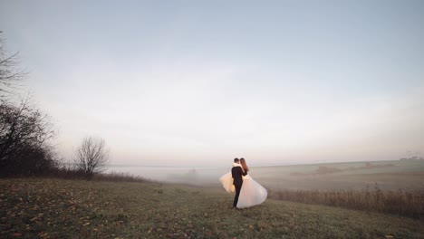 Newlyweds-dancing.-Caucasian-groom-with-bride-on-the-morning-field.-Fog.-Wedding