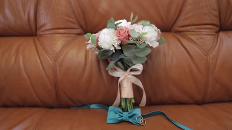 Beautiful-wedding-bouquets-lie-with-wedding-rings-and-grooms-bow-tie-on-sofa