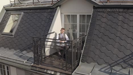 Man-groom-businessman-is-drinking-coffee-from-a-white-cup-on-the-balcony-at-home-in-wedding-morning