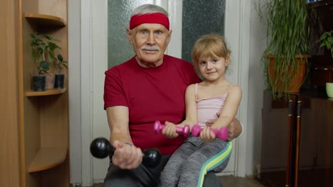 Child-kid-girl-with-senior-grandfather-in-sportswear-making-sports-workout-exercises-with-dumbbells