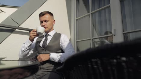 Man-groom-businessman-is-drinking-coffee-from-a-white-cup-on-the-balcony-at-home-in-wedding-morning