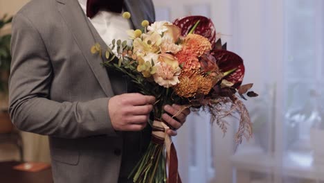 Groom-with-wedding-bouquet-in-his-hands-at-home-preparing-to-go-to-bride,-close-up,-slow-motion