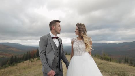 Lovely-young-newlyweds-bride-groom-walking-on-mountain-slope,-making-a-kiss,-wedding-couple-family