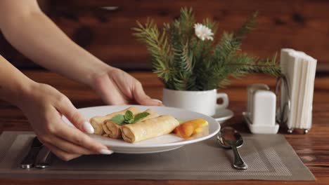 Hands-of-waiter-puts-white-plate-with-delicious-vegan-banana-peach-pancakes,-breakfast-in-restaurant