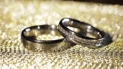 Wedding-rings-lying,-rotate,-spinning-on-shiny-golden-shining-surface-with-light,-close-up-macro