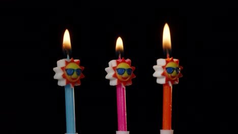 Birthday-festive-candles-in-form-of-sun-in-sunglasses-turning,-spinning-isolated-on-black-background