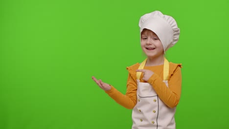 Child-girl-dressed-cook-chef-baker-in-apron-pointing-at-left-on-blank-space-on-chroma-key-background