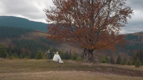 Lovely-newlyweds-bride-groom-dancing-on-mountain-autumn-slope,-wedding-couple-family,-aerial-view