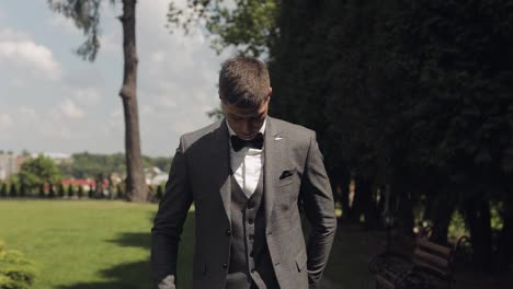 Groom-goes-down-the-alley-between-bushes-with-a-wedding-bouquet-to-his-beloved-bride,-first-meeting