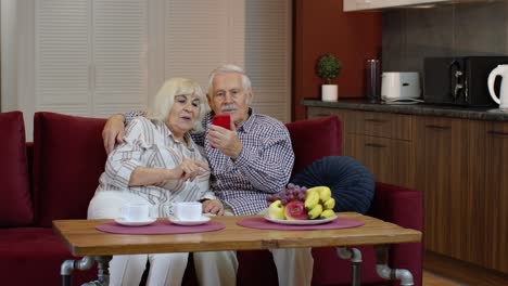 Grandmother-and-grandfather-making-video-call-online-on-mobile-phone-at-home.-Smiling-senior-couple