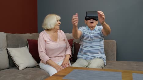 Grandfather-and-grandmother-with-VR-headset-helmet-play-games,-watch-virtual-reality-3D-360-video