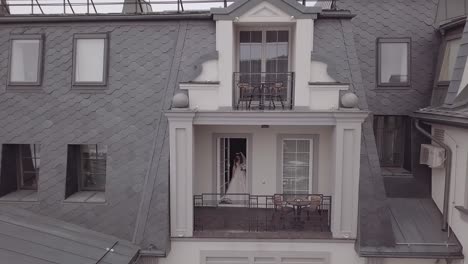 Bride-in-wedding-dress-on-balcony-of-her-house.-Wedding-morning.-Aerial-view