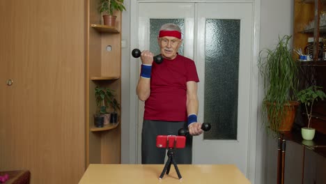 Senior-elderly-mature-man-watching-online-distance-workout-exercises-with-dumbbells-on-mobile-phone