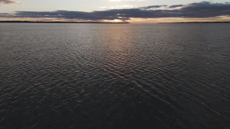 Toma-Aérea-Desde-El-Agua-Hacia-La-Puesta-Del-Sol