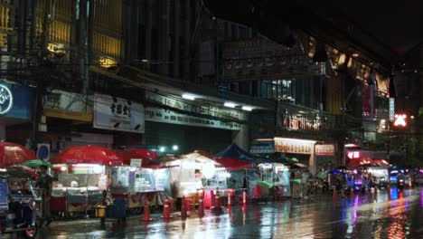 Vibrante-Mercado-Nocturno-Bajo-La-Lluvia-En-Chinatown,-Bangkok,-Con-Luces-De-Colores-Y-Vendedores-Ambulantes-De-Comida