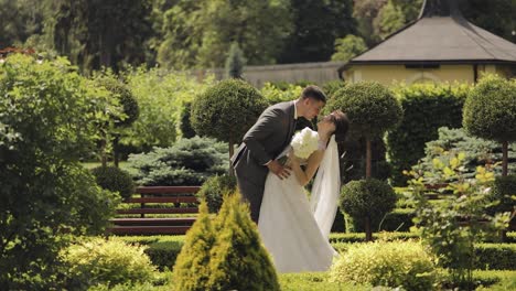 Newlyweds,-caucasian-groom-with-bride-walking,-embracing,-hugs-making-a-kiss-in-park,-wedding-couple