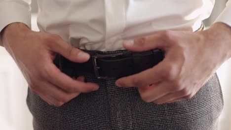 Groom-wears-belt,-man-in-white-shirt-puts-belt-on-pants-in-wedding-morning,-businessman-preparation