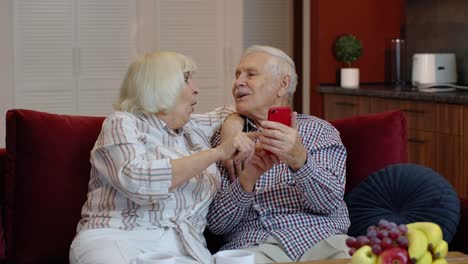 Abuelos-De-Una-Pareja-De-Ancianos-Hablando-Y-Usando-Una-Computadora-De-Teléfono-Móvil-En-Casa.-Compras-Por-Internet