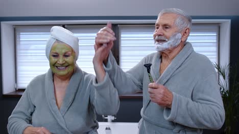 Senior-couple-man-and-woman-in-bathrobe-are-dancing-in-bathroom-having-fun-enjoying-leisure-time