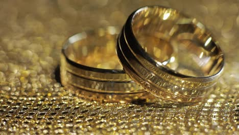 Wedding-gold-rings-lying-on-shiny-glossy-surface.-Shining-with-light.-Close-up