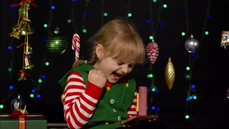 Kid-girl-in-Christmas-elf-costume-doing-shopping-online-using-mobile-phone,-browsing-on-social-media