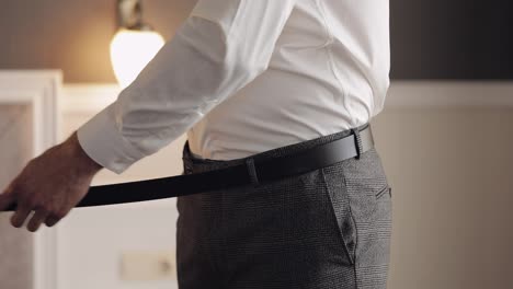 Groom-wears-belt,-man-in-white-shirt-puts-belt-on-pants-in-wedding-morning,-businessman-preparation