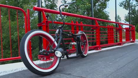 Footage-of-a-black-chopper-styled-bike-or-a-bicycle-with-whitewall-wheels-and-red-rims-on-a-bridge-with-red-railings