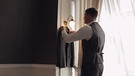 Handsome-groom-businessman-taking-and-preparing-to-wear-gray-jacket-at-home-in-living-room