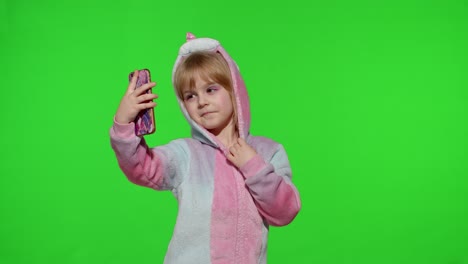 Child-girl-in-unicorn-costume-pajamas-using-smartphone,-kid-emotionally-makes-selfie-on-mobile-phone