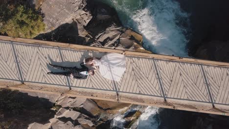 Frischvermählte.-Braut-Und-Bräutigam-Liegen-Auf-Einer-Brücke-über-Einem-Gebirgsfluss.-Luftaufnahme