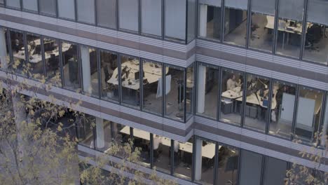 Evening-view-of-a-modern-office-building-with-workers-at-their-desks,-visible-through-large-windows