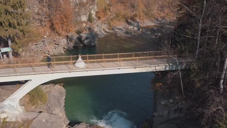 Frischvermählte.-Braut-Und-Bräutigam-Auf-Einer-Brücke-über-Einem-Gebirgsfluss.-Luftaufnahme