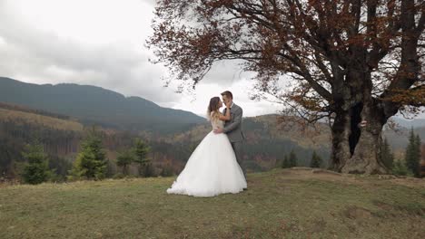 Lovely-young-newlyweds-bride-and-groom-embracing,-making-a-kiss-on-mountain-slope,-wedding-couple